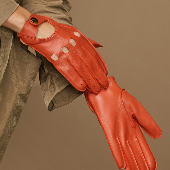 Women's orange lambskin glove close-up with touchscreen panel on thumb