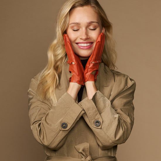 Women's orange lambskin driving gloves on hands, perforated touchscreen fingertips
