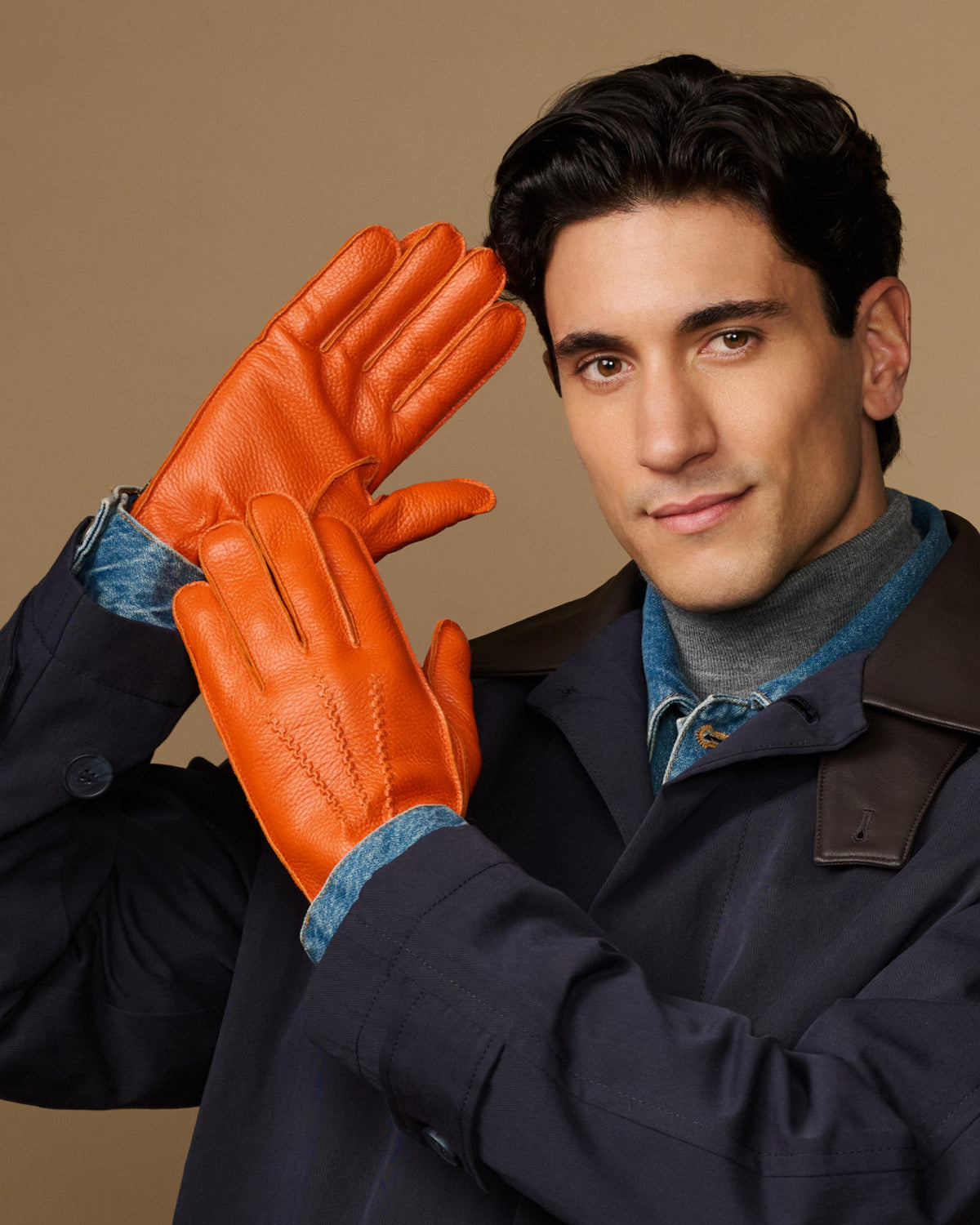 Men’s orange leather gloves with blue lining cuff, hand posed forward