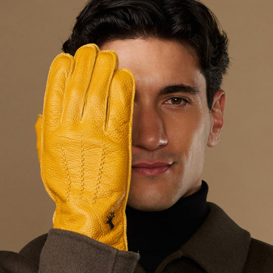 Yellow leather glove close-up on model’s hand, fingers and grain texture visible