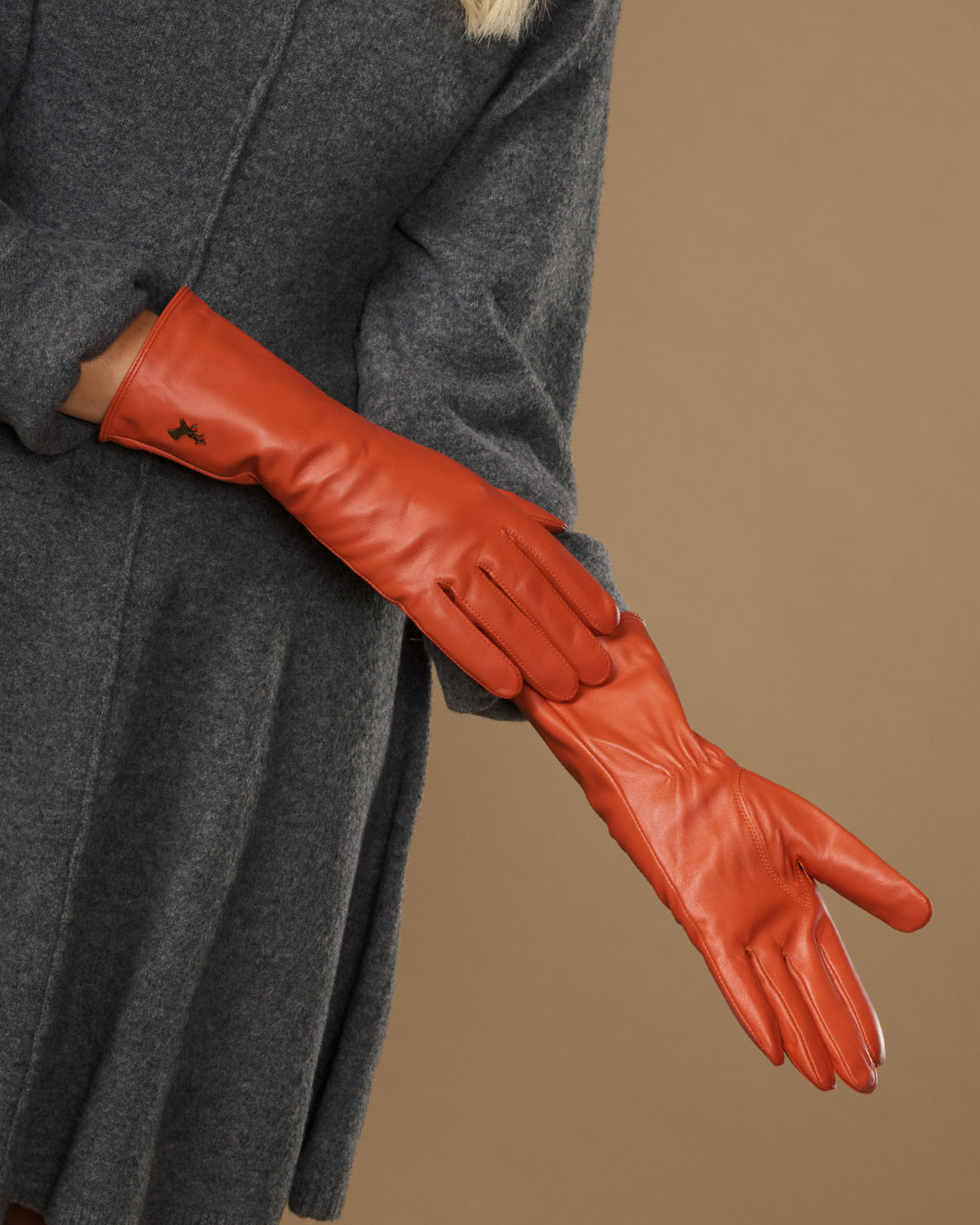 Orange long leather glove laid over sleeve, showing stitched finger panels