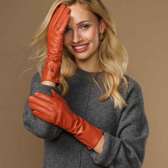 Orange leather gloves worn near face, long cuffs visible with finger stitching