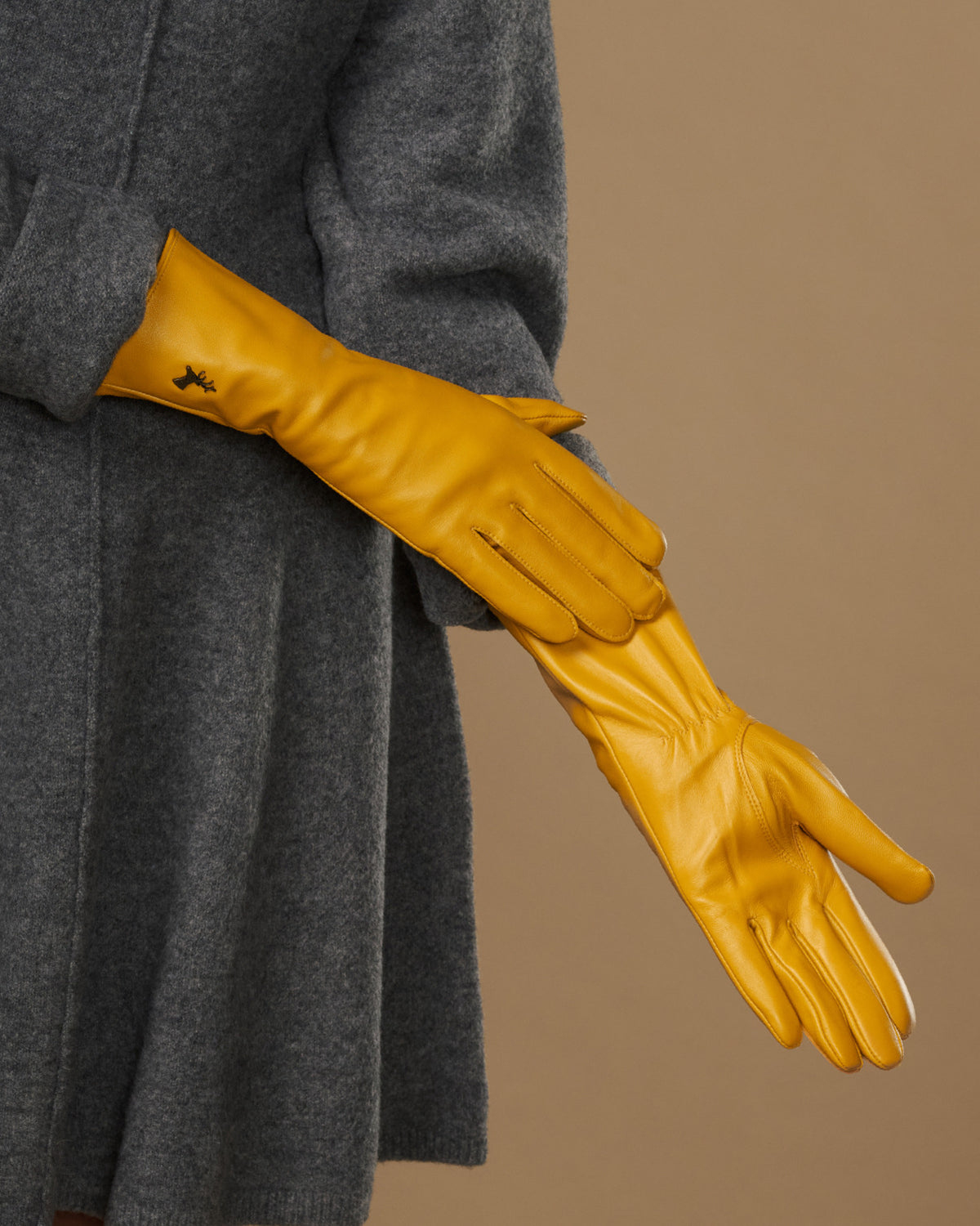 Yellow extra-long leather gloves stretched forward; cuff logo and seam details