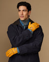 Men's yellow lambskin driving gloves worn with a navy coat, perforated knuckles