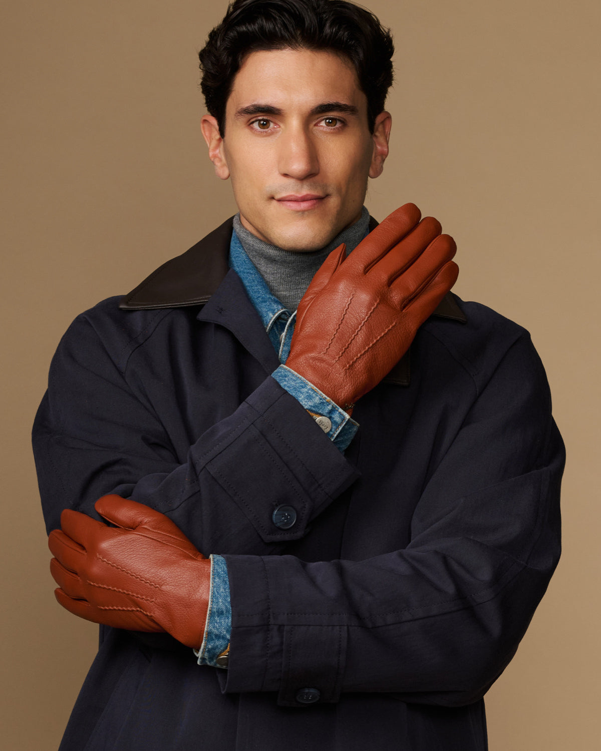 Cognac leather gloves with blue wool lining cuff, one hand raised