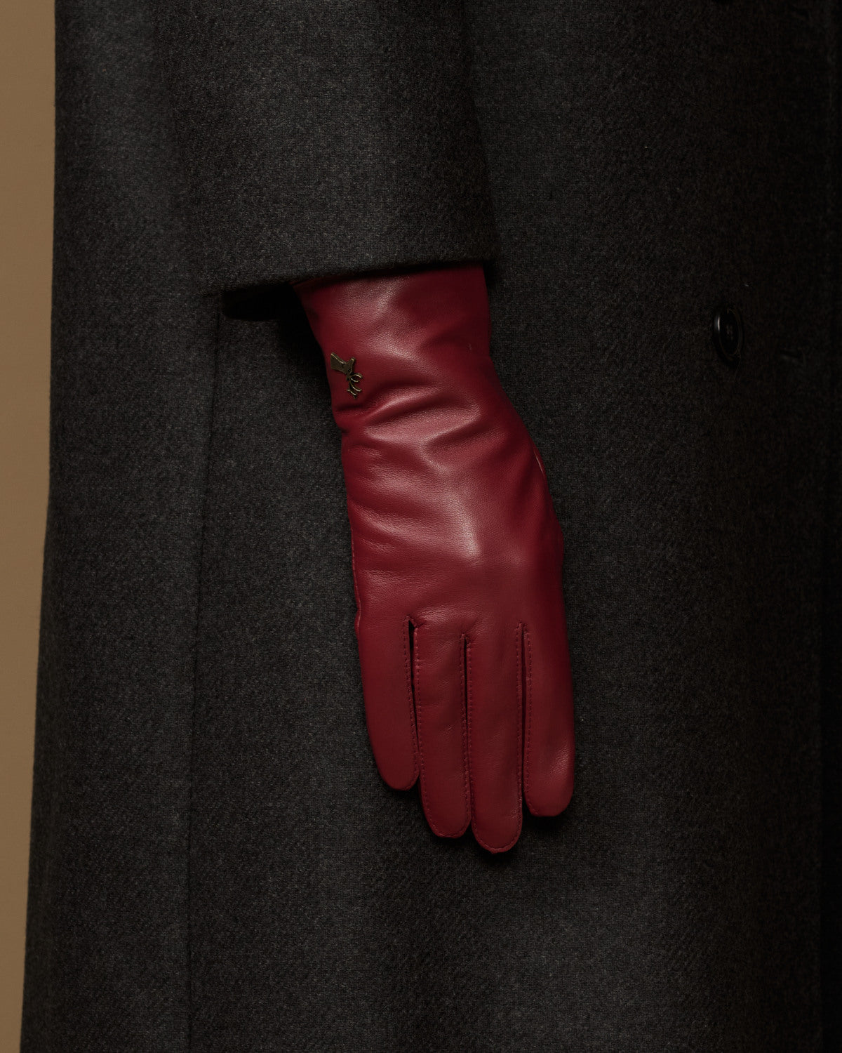 Bordeaux leather glove showing from a dark coat sleeve with stitched cuff