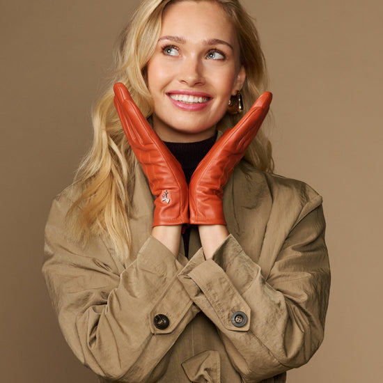 Orange sheepskin leather gloves with fleece lining, worn with hands raised near face