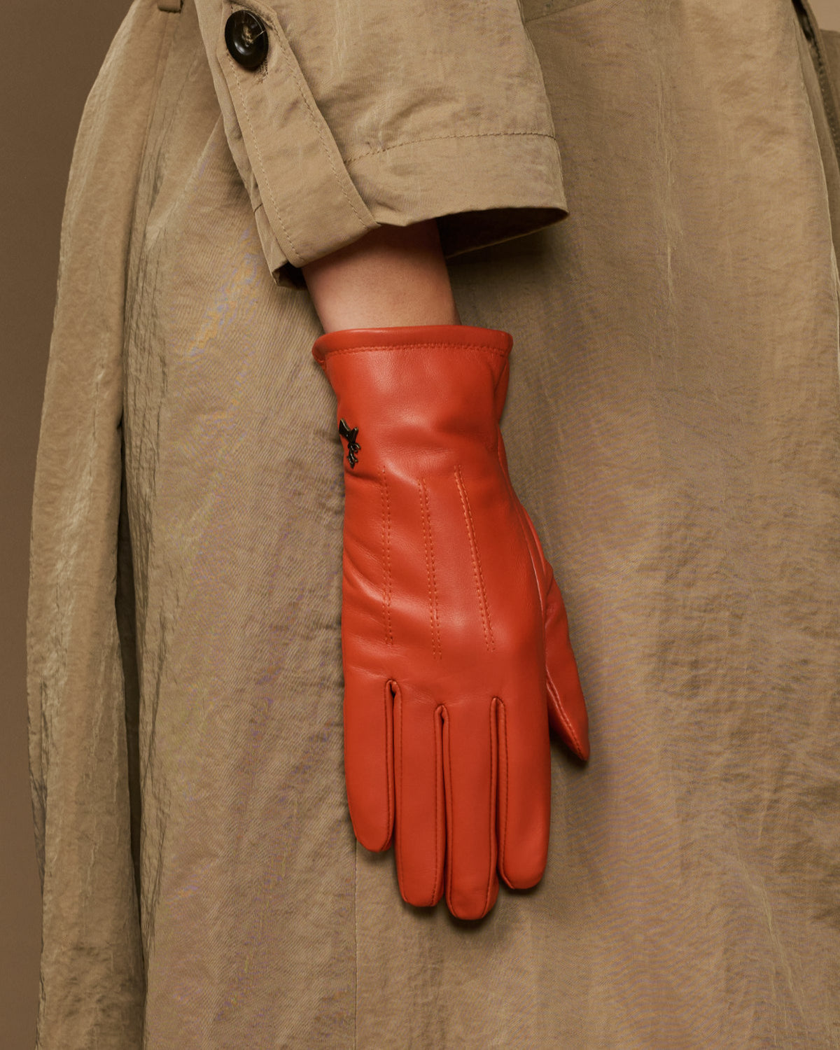 Orange sheepskin leather glove with fleece lining, hanging from a jacket cuff