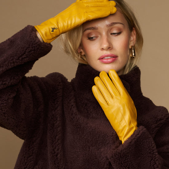Yellow leather gloves with dark fleece cuff, held up near the face
