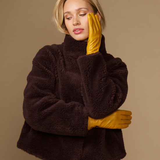 Yellow leather gloves with fleece-lined cuff, arms crossed while wearing a coat