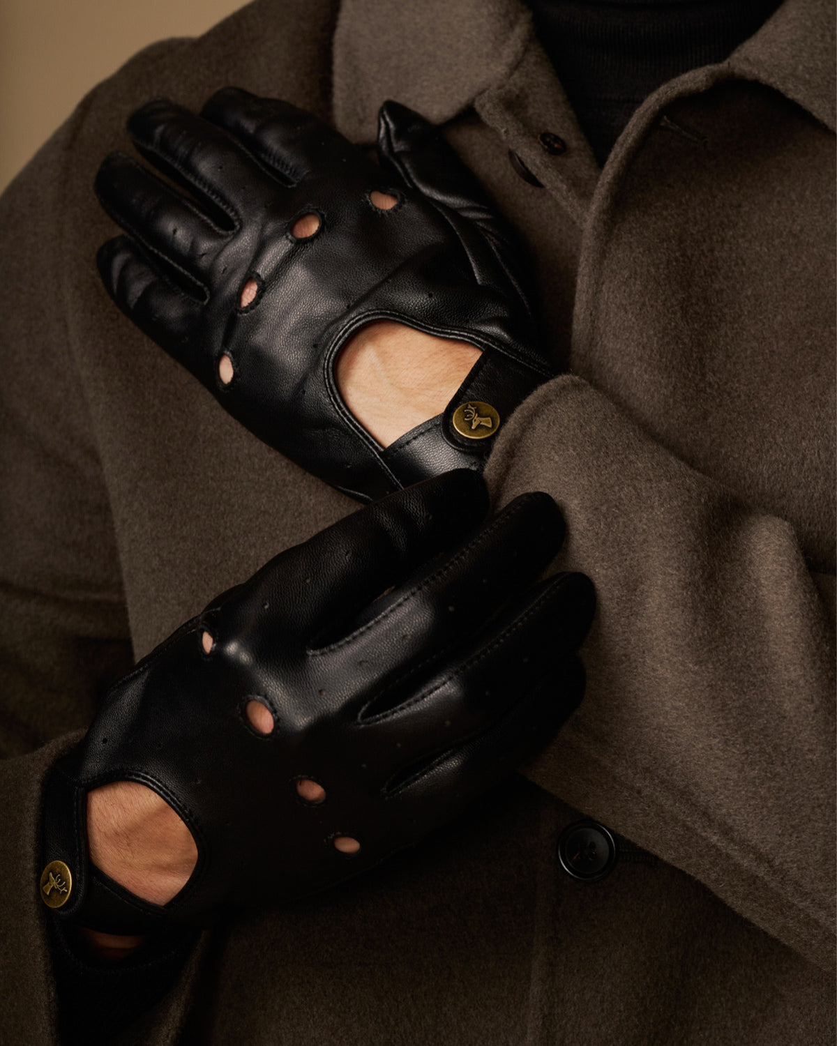 Close-up of black leather driving gloves with stud details and touchscreen thumb panel