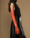 Orange leather gloves with fitted cuffs; silk lining and touchscreen feature visible on wrist