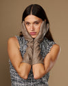 Taupe below-elbow leather gloves framing face in front view, smooth back and stitched fingers.