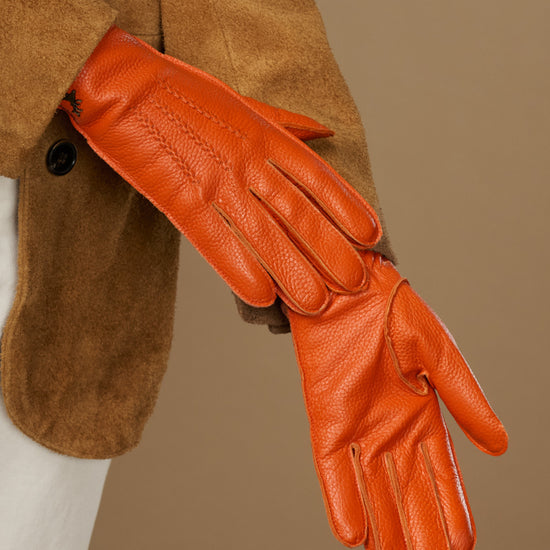 Orange leather glove close-up with textured stitching on knuckles and palm, extended hand